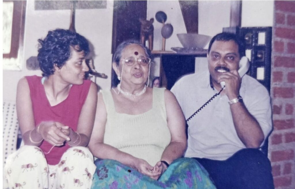 A black and white photograph of a 1990 viewer, showing writer Arundhati Roy in the same frame with her mother and brother. All three of them are sitting.
ভালোবাসা